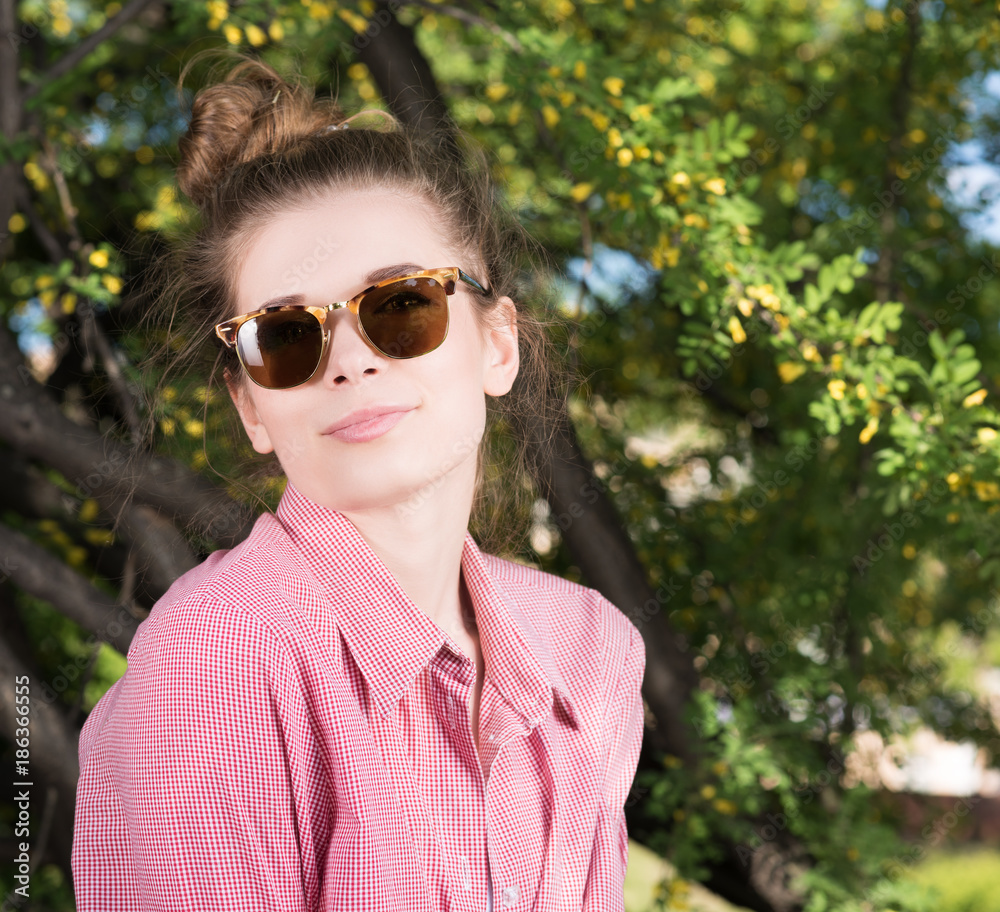 Cute young woman wearing sunglasses outdoors. Pink shirt, hair wrapped