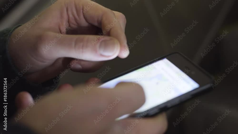 A man is riding an escalator in the subway. Man searches location on map in phone. Close-up.