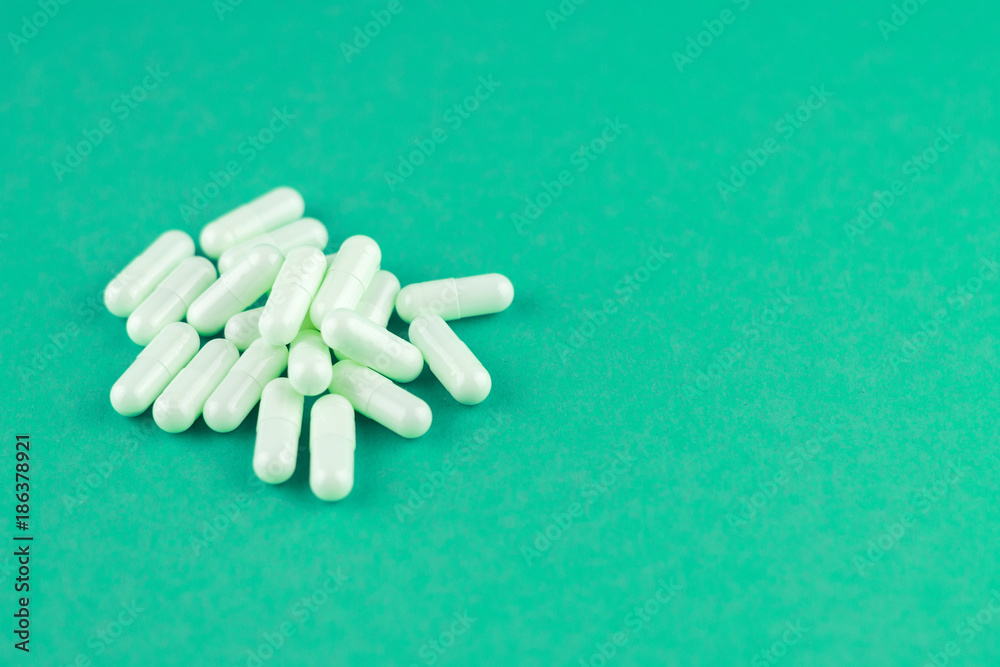 Close up white capsules on emerald green background with copy space. Focus on foreground, soft bokeh. Pharmacy drugstore concept Close up white capsules on emerald green background with copy space. Focus on foreground, soft bokeh. Pharmacy drugstore concept