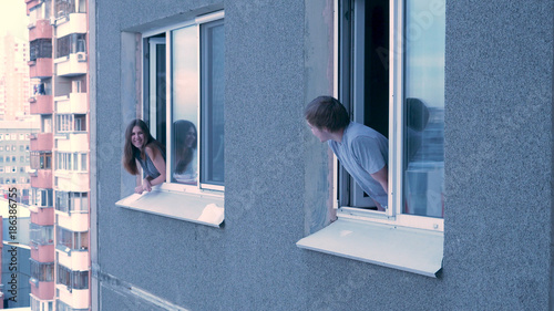 Neighbors talk to each other from the window. Young happy couple conversing in window. Neighbors concept. Young couple having a conversation while looking at each other over a window background photo