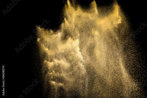 Golden sand explosion isolated on black background. Abstract sand cloud. Golden colored  sand splash agianst  dark background. Yellow sand fly wave in the air. photo