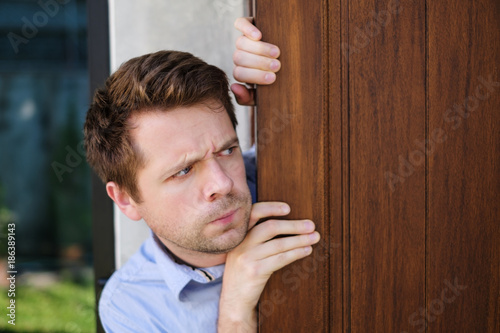 Young caucasian man with agoraphobia spying and looking out the door.