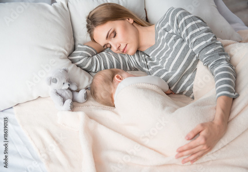 Daytime sleep. Calm mom with lovely daughter napping on cozy bed at home