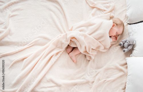 Top view of little baby covered with blanket sleeping on soft bed. She is suckling her thumb. Copy space in left side photo