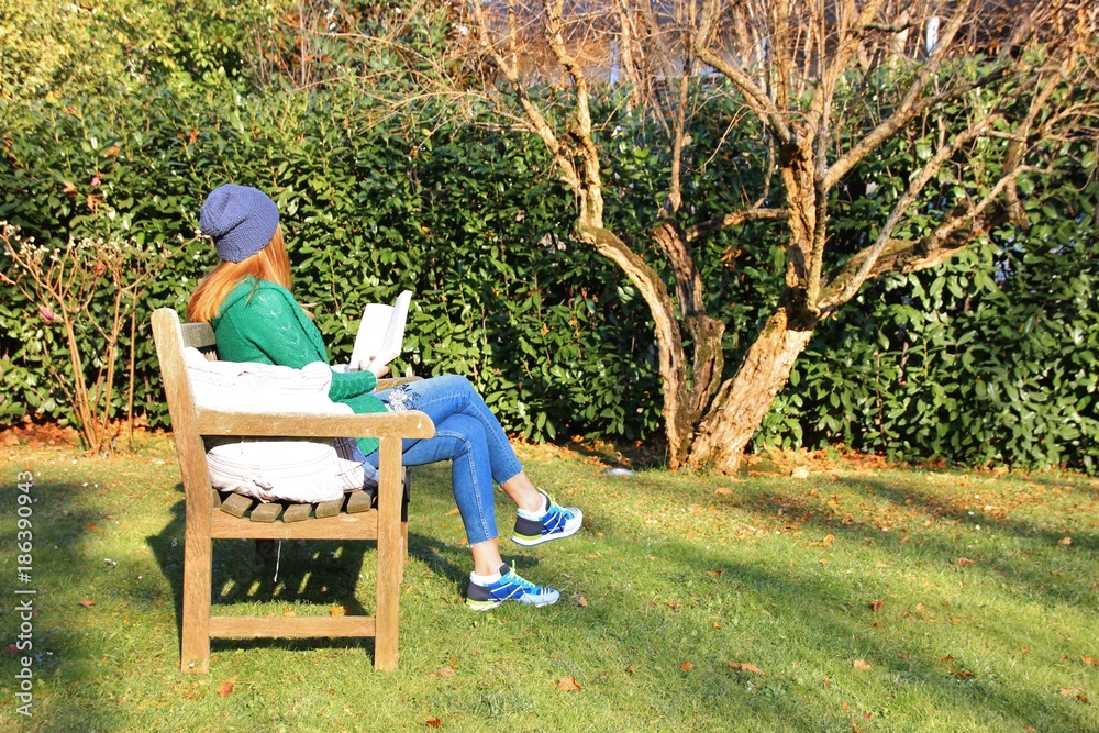 Girl reading a book on a wooden bench in a park. Italy Girl reading a book on a wooden bench in a park. Italy