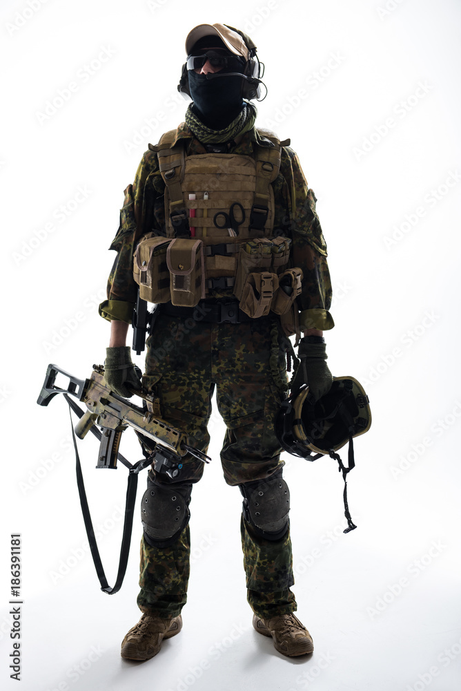 Fototapeta premium Full length portrait of serious peacemaker holding helmet and modern weapon in arms. Army concept