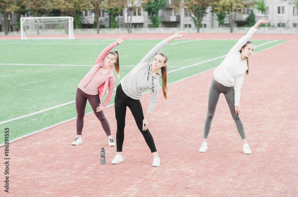 Fototapeta premium Three girls doing aerobic exercises at the football stadium