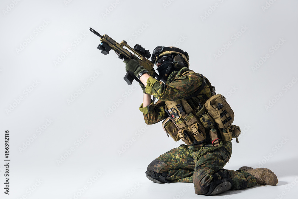 Side view severe soldier shooting with assault rifle while locating on knees. Tactic concept. Copy space Side view severe soldier shooting with assault rifle while locating on knees. Tactic concept. Copy space