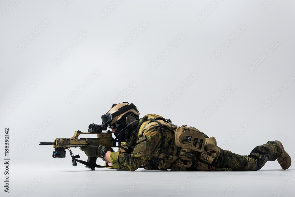 Full length side view serene peacemaker looking at sniper scope of assault rifle while locating at ground. Army concept. Copy space Full length side view serene peacemaker looking at sniper scope of assault rifle while locating at ground. Army concept. Copy space