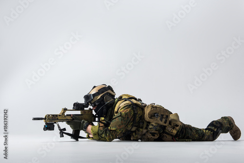 Full length side view serene peacemaker looking at sniper scope of assault rifle while locating at ground. Army concept. Copy space