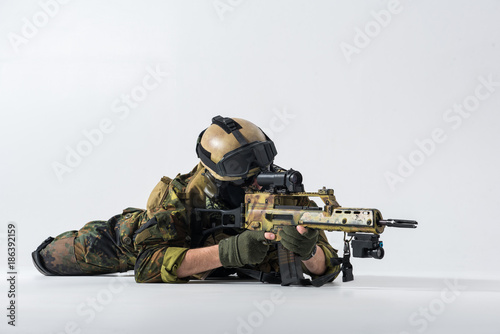 Portrait of severe soldier looking at sniper scope of modern assault rifle while locating at floor. Army concept. Copy space