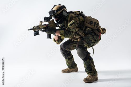 Side view full length concentrated soldier shooting with assault carbine at war. Protection concept