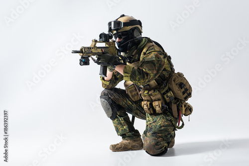 Portrait of orderly soldier looking at sniper scope of modern assault rifle. War concept