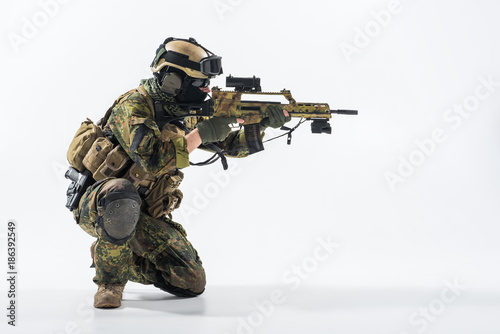 Side view stern soldier looking at sniper scope while shooting with assault carbine. War concept. Copy space
