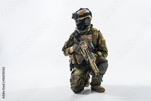 Serious peacemaker in army uniform looking away while holding weapon. Protection concept. Copy space