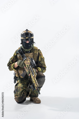 Portrait of serene soldier in balaclava and helmet while kneeling and keeping assault rifle. Patriotism concept