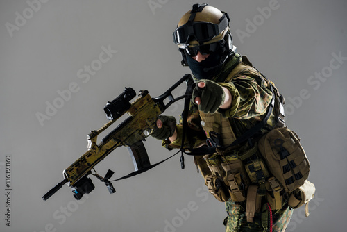 Hey you. Portrait of orderly man pointing in camera by finger. He wearing body armor and holding assault rifle in hands. Army concept