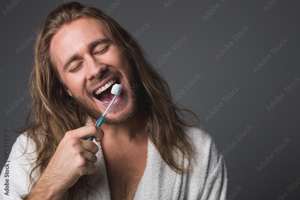 Portrait of joyful bearded man brightening his teeth with eyes closed. Isolated on grey background Portrait of joyful bearded man brightening his teeth with eyes closed. Isolated on grey background