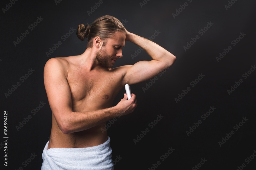 Obraz premium Naked man in the towel using antiperspirant. Isolated on black background. Copy space in right side