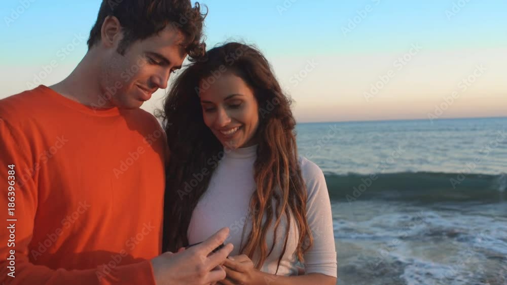 Young couple standing beach in sunset taking photograph Young couple standing beach in sunset taking photograph
