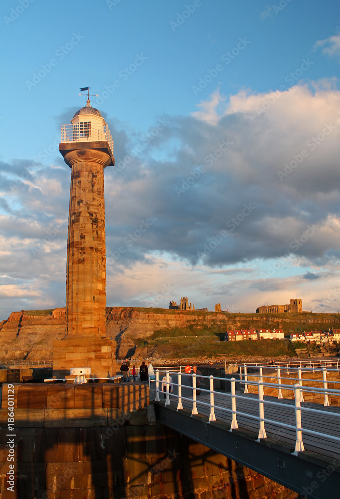 The setting sun at Whitby lights up the lighthouse and in the distance the ancient Whitby Abbey.