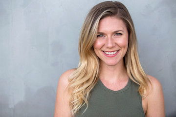 Gorgeous headshot of young bright cheerful sincere smiling caucasian blond female against a gray background