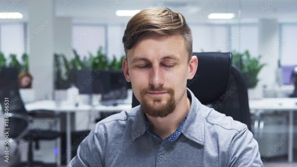 Business man with a beard turns his head to the camera and smiling, office interior as background