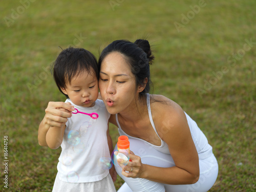 asian chinese female parent blowing bubbles with baby girl