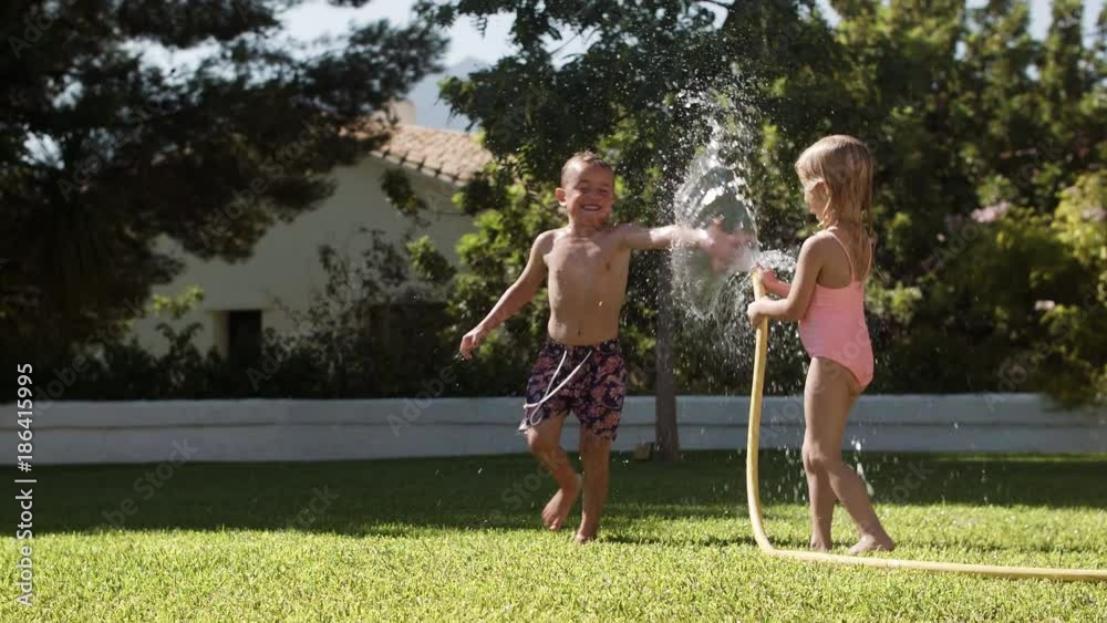 Two children playing with water hose in garden Two children playing with water hose in garden