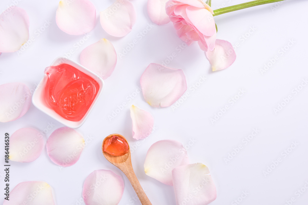 Spa accessories in Pink. Top view of body cream and pink rose flower petals on white background.