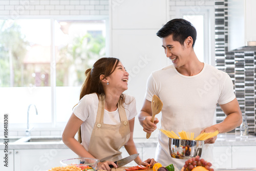 Young asian woman cutting slice vegetables making salad healthy food with fruits and man cooking menu for dinner in kitchen at home fun couple together romantic