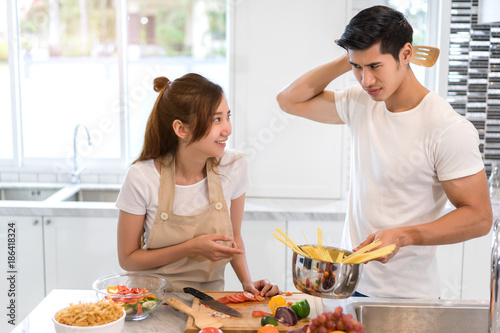 Young asian woman cutting slice vegetables making salad healthy food with fruits and man cooking menu for dinner in kitchen at home fun couple together romantic