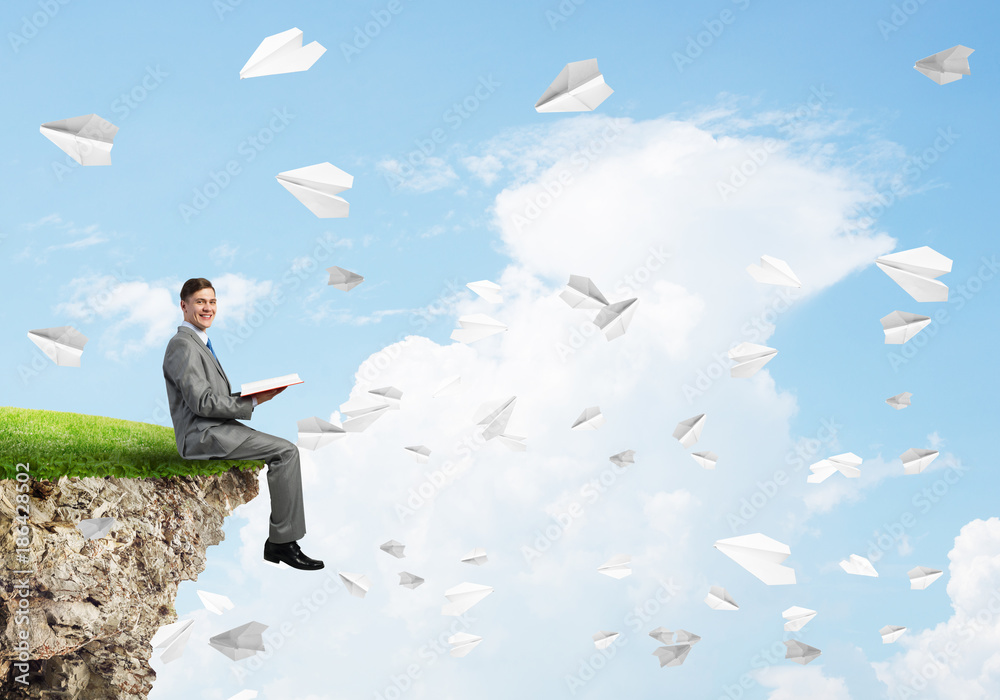 Man on edge reading book and paper planes flying in air Man on edge reading book and paper planes flying in air