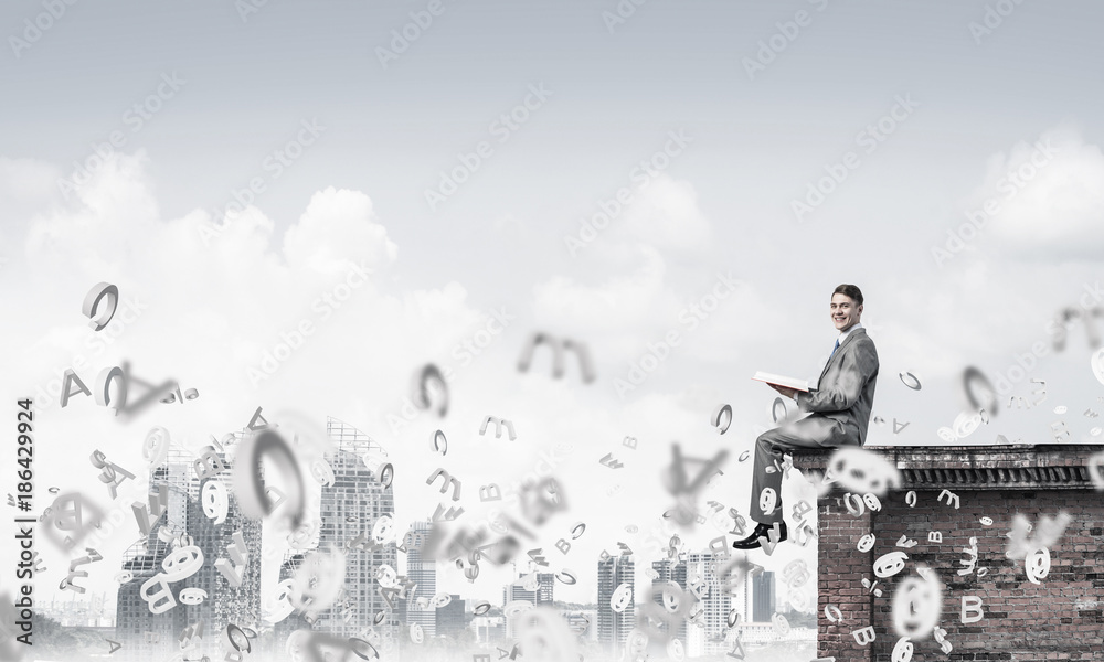 Man on roof edge reading book and symbols flying around Man on roof edge reading book and symbols flying around