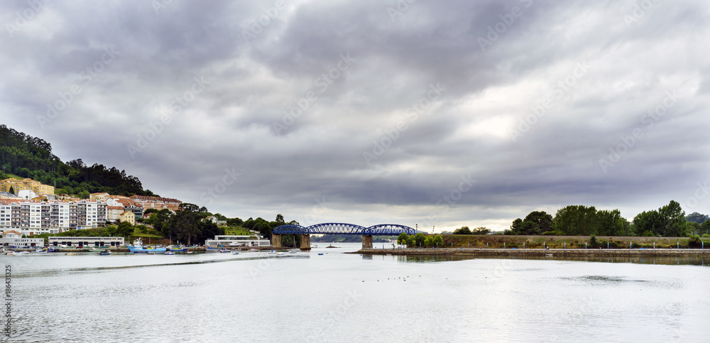 View of the Eume river with an iron bridge for the railway and part of the town of Pontedeume in Galicia, Spain. Sky covered with clouds threatening rain