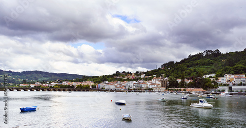 View of the Eume estuary with the stone bridge that crosses it to the bottom and anchored pleasure boats. The village of Pontedeume, Galicia, Spain in the background and a sky covered with clouds
