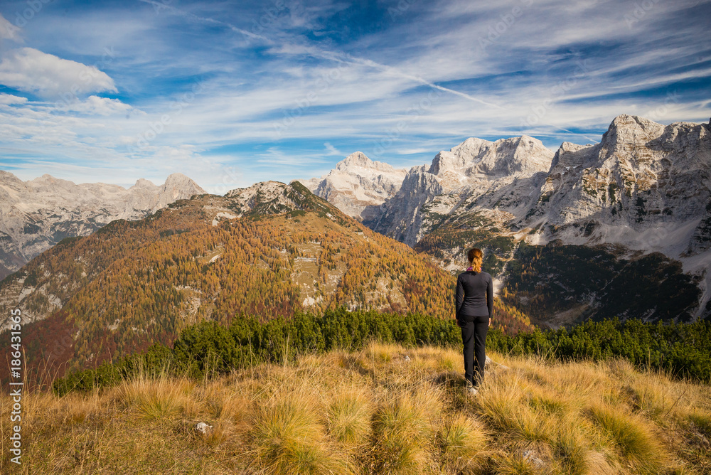 Young female is admiring mount Triglav and Julian alps in autumn colors from a mountain top in Triglav National Park, Slovenia