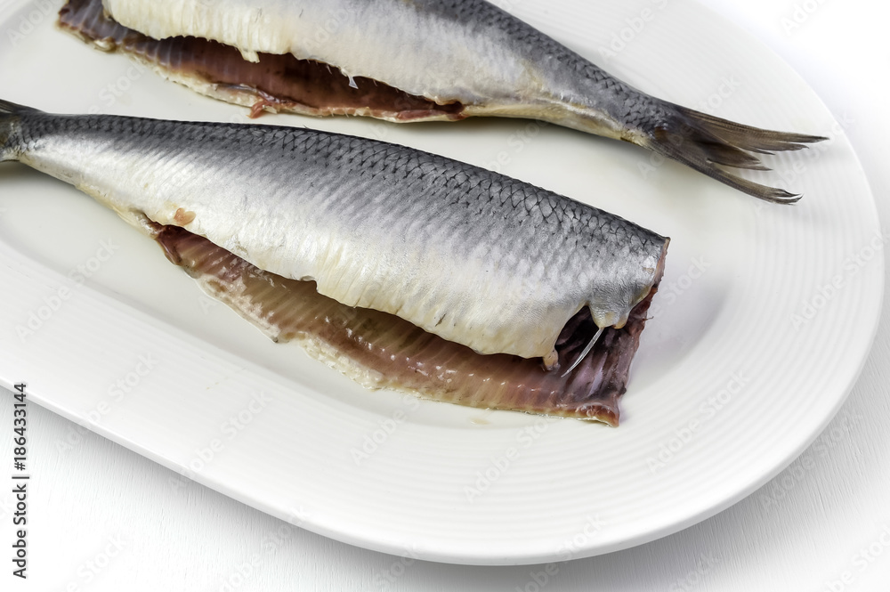 Salted herrings without head on the plate, isolated on white background. Salted herrings without head on the plate, isolated on white background.