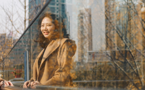 The mirror image of a beautiful Chinese girl, smiling and looking at herself with modern city building background.