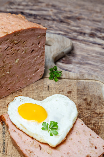 Einfache Hausmannskost mit Herz- Leberkäse und Spiegelei auf rustikalem Holztisch mit viel Textfreiraum photo