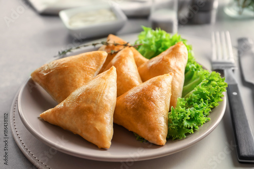 Plate with delicious baked samosas on table