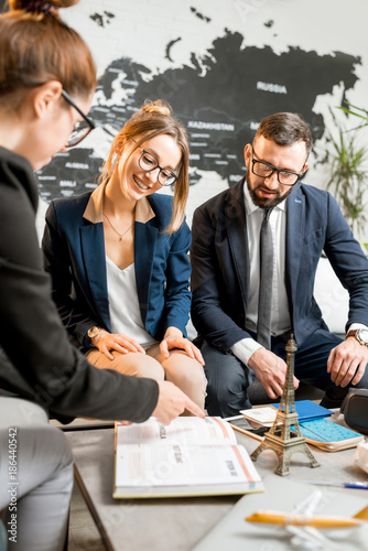 Young businesscouple choosing a trip with agent sitting at the travel agency office with world map on the background photo