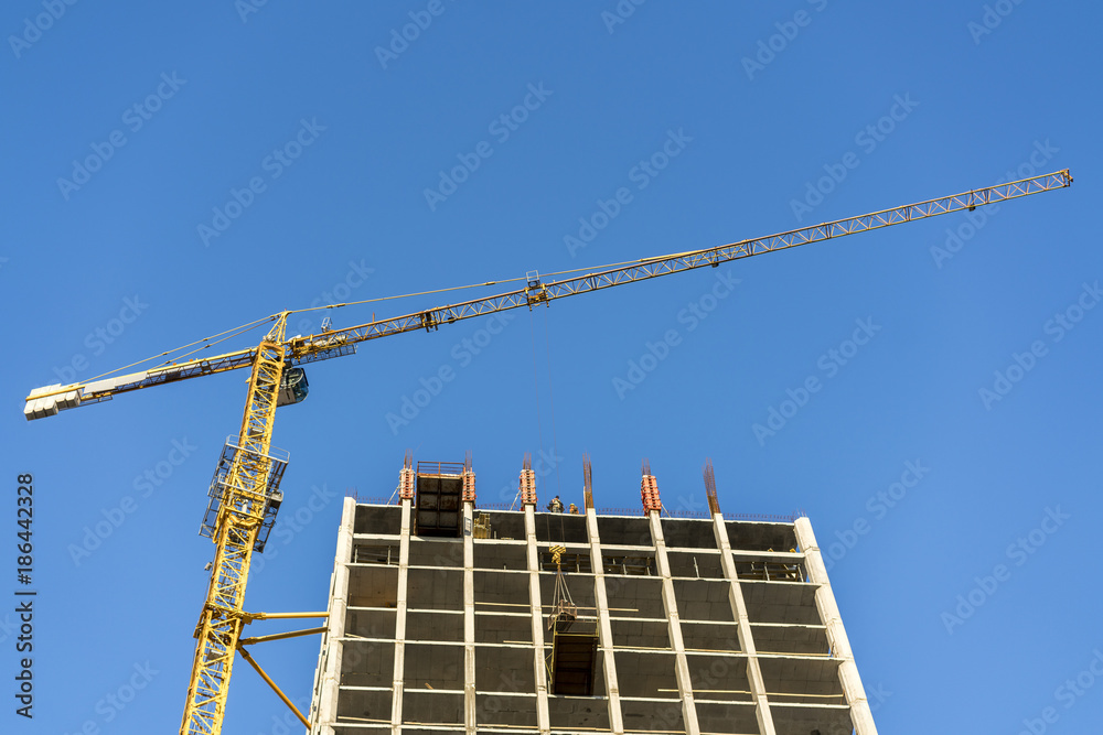 Construction of a high-rise building. Crane, builders against the blue sky
