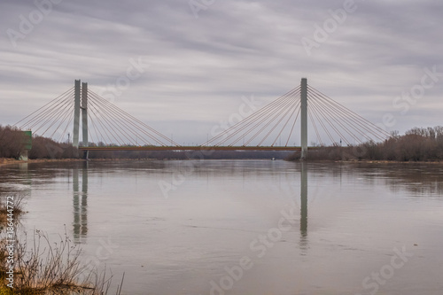 Water landscape with the suspension bridge across the Vistula river and its reflection in water under the cloudy sky