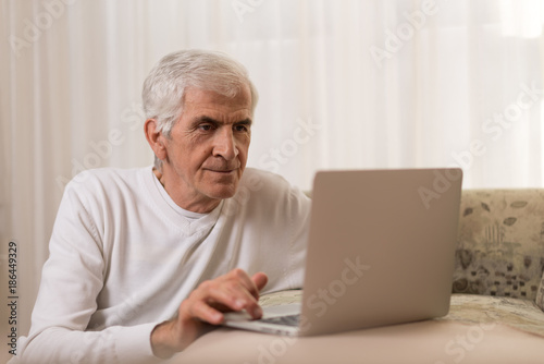 Senior man using laptop at home and surfing the net