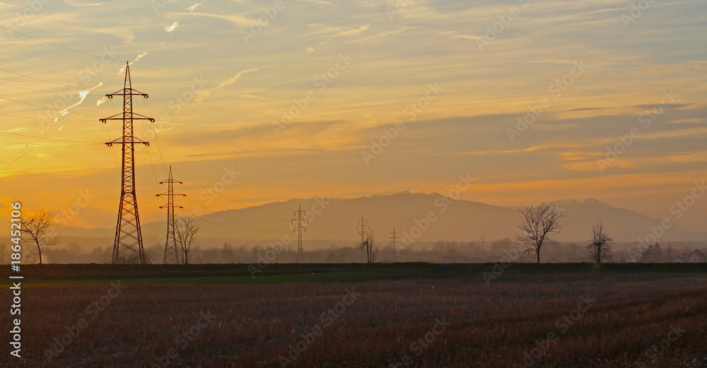landscape with pylons of electric wiring and the hills at the background in the evening