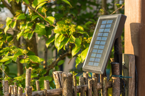 Solar panel in the graden, providing three led-lights with renewable energy. Green energy souce for garden lamps. Soalr panel, fixed on the brown garden fence with willow wood. photo