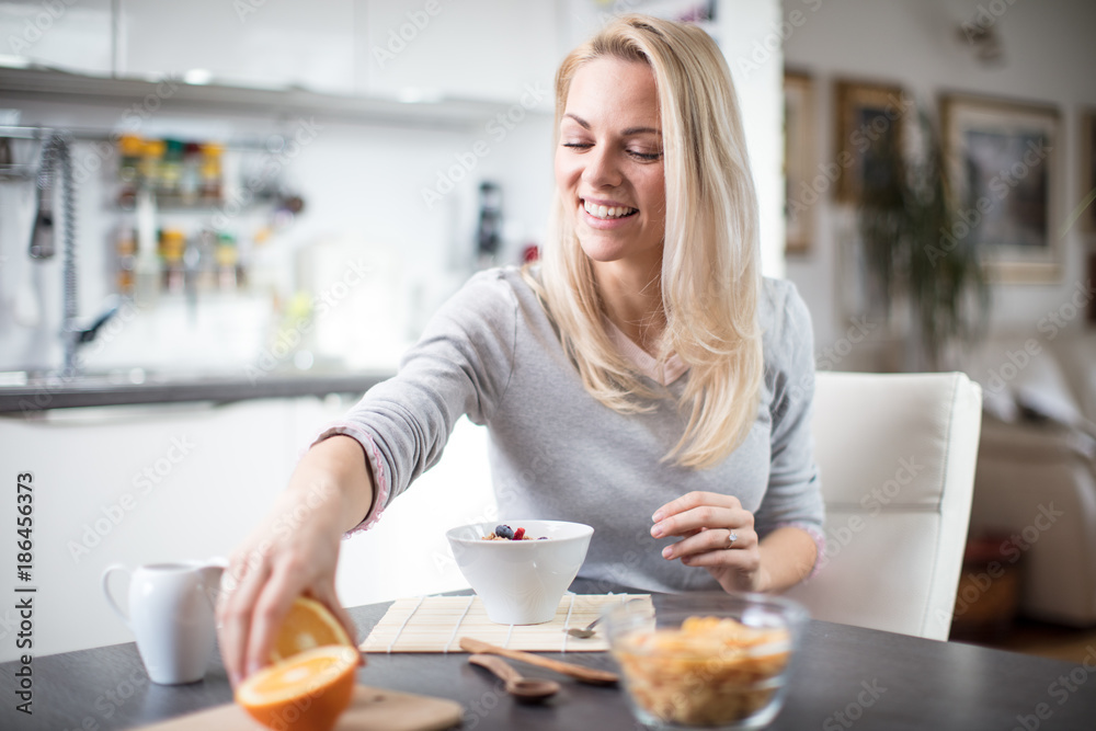 Beautiful blond caucasian woman posing in her kitchen, while drinking coffee or tea and eating a healthy breakfast meal full of cereal and other healthy foods, including fruit Beautiful blond caucasian woman posing in her kitchen, while drinking coffee or tea and eating a healthy breakfast meal full of cereal and other healthy foods, including fruit