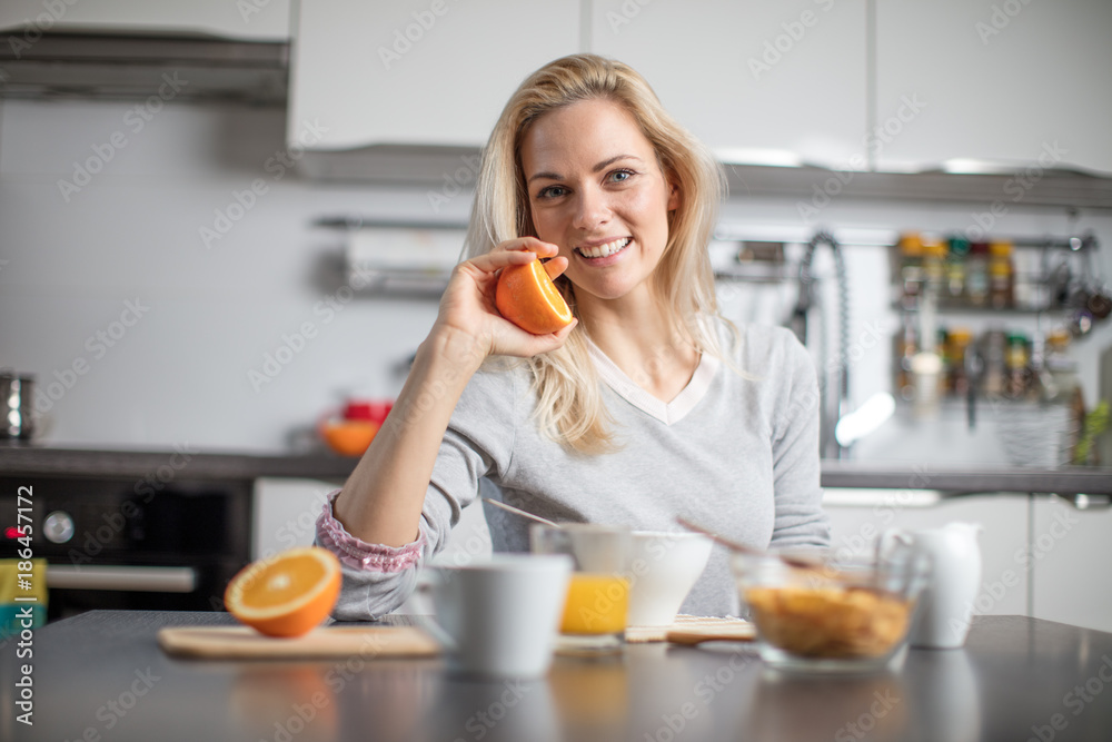 Beautiful blond caucasian woman posing in her kitchen, while drinking coffee or tea and eating a healthy breakfast meal full of cereal and other healthy foods, including fruit Beautiful blond caucasian woman posing in her kitchen, while drinking coffee or tea and eating a healthy breakfast meal full of cereal and other healthy foods, including fruit