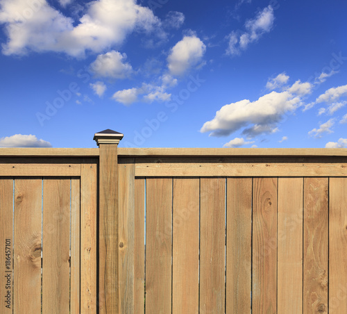 New, contemporary wood fence with blue sky and clouds in the background